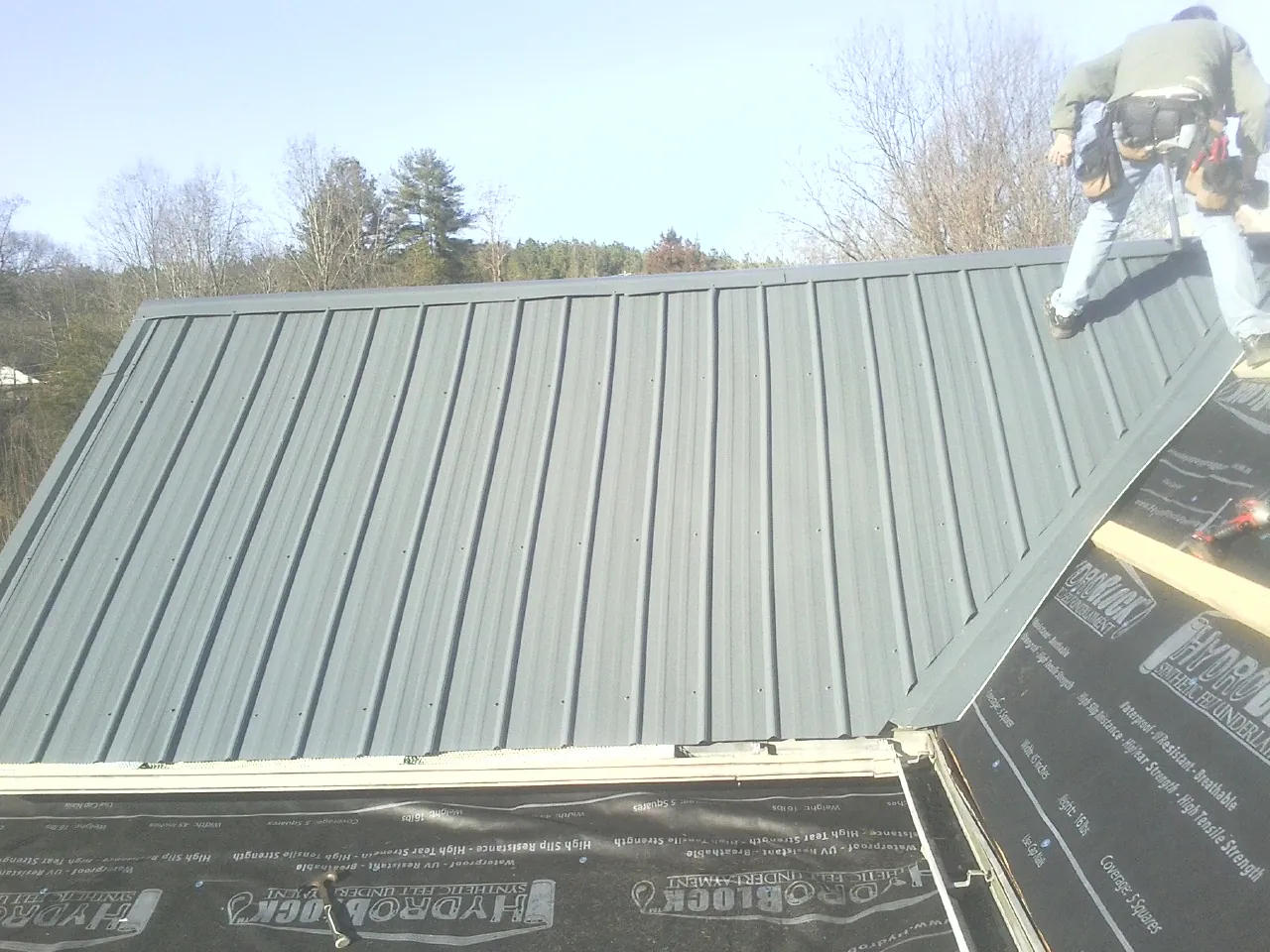 Crew installing dark green standing seam panels over synthetic underlayment in Montebello
