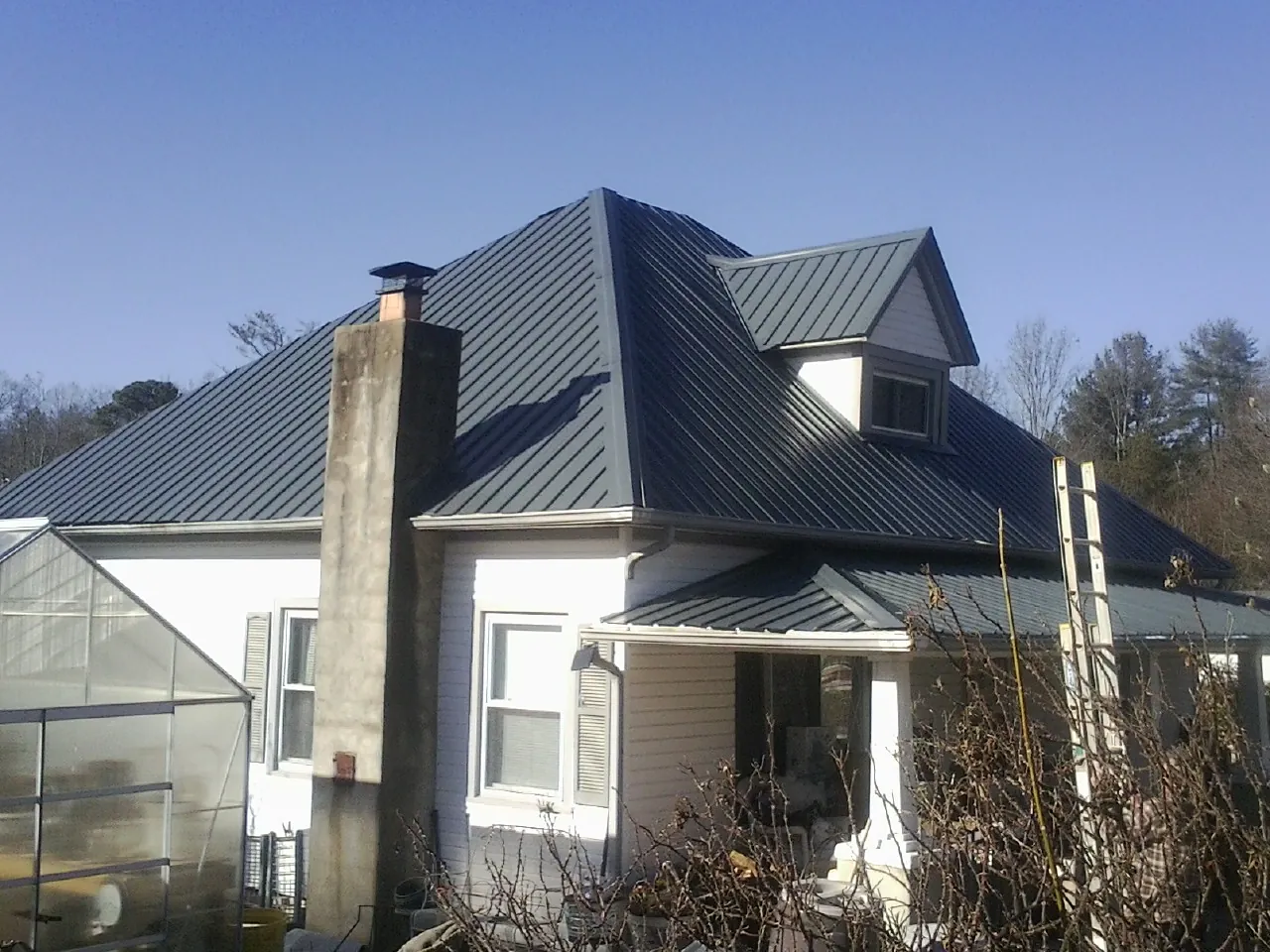 Dark blue standing seam metal roof on a white farmhouse with dormer — Slate & Tile Roof Repair by Roofing Brothers in Montebello