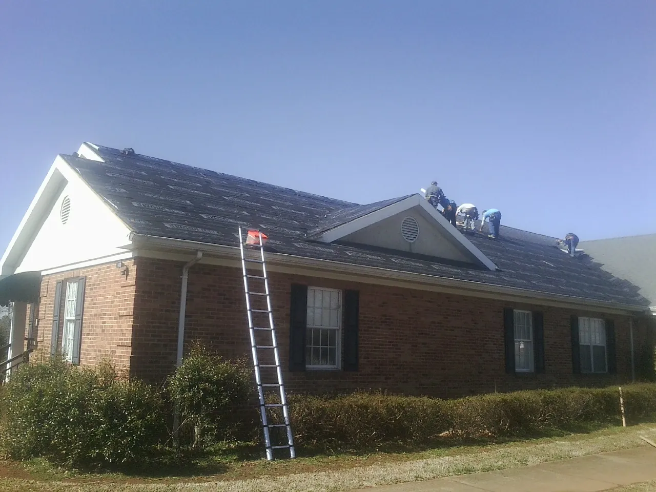 Crew tearing shingles off a brick ranch roof with a ladder set — Emergency Roof Repair work by our crew in Montebello