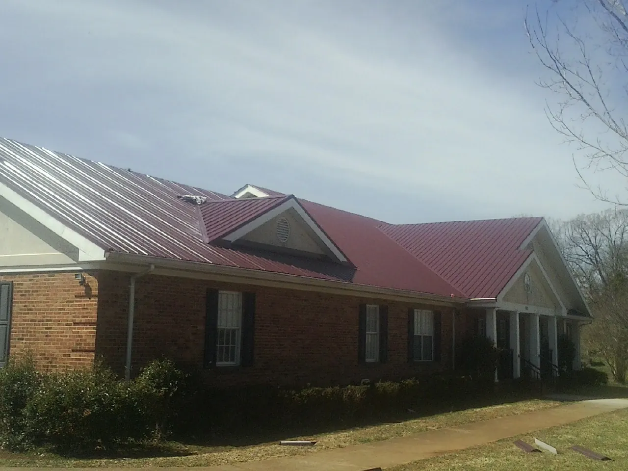 Red metal roof with gabled entries on a long brick building, from a Hail Damage Roof Repair job in Montebello