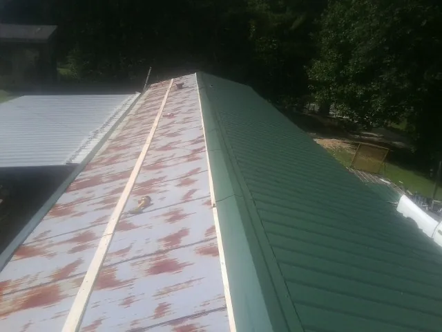 Old rusted panels beside newly installed green metal roofing — Wind Damage Roof Repair by Roofing Brothers in Montebello