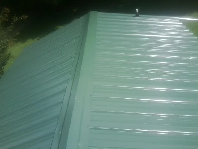New green metal panels meeting at the ridge of a roof — Flat Roof Repair work by our crew in Montebello